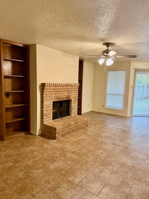 9006 B Sedgemoor Trail Austin, TX 78748 - Photo 6 of 16 Unfurnished living room with built in features, a brick fireplace, a textured ceiling, and a ceiling fan