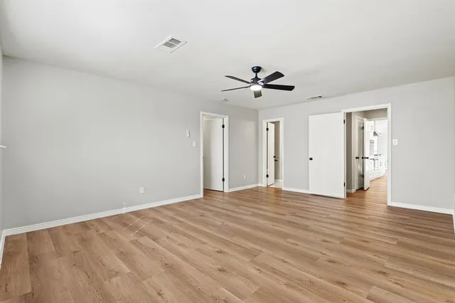 a view of an empty room with wooden floor and a ceiling fan