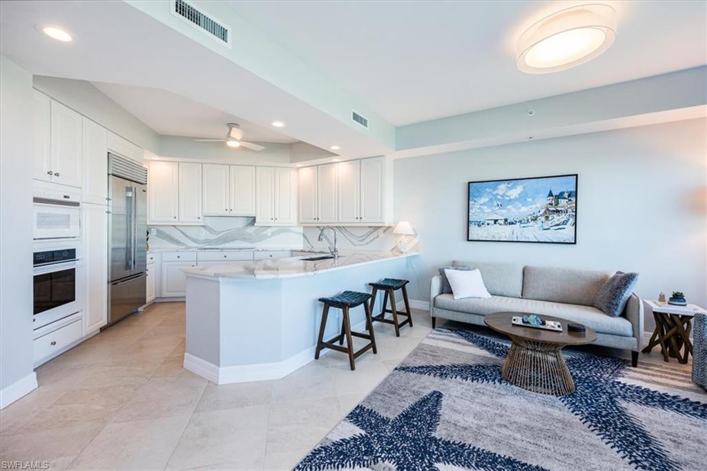 295 Grande Way, Unit 702 Naples, FL 34110 - Photo 5 of 31 a living room with white couches and kitchen view with wooden floor