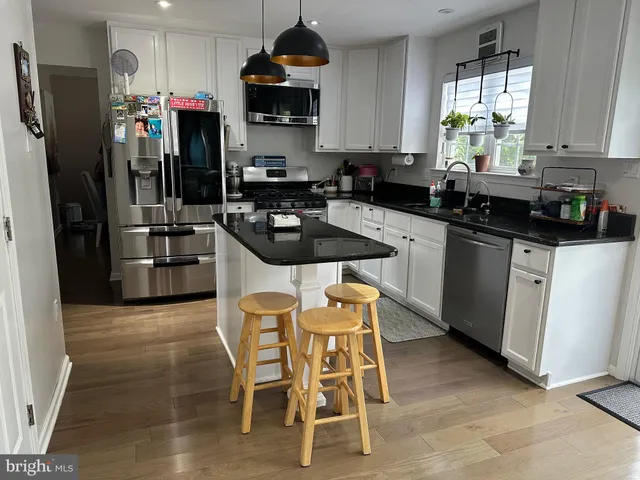 a kitchen with stainless steel appliances granite countertop a sink a stove a refrigerator cabinets and a dining table with wooden floor