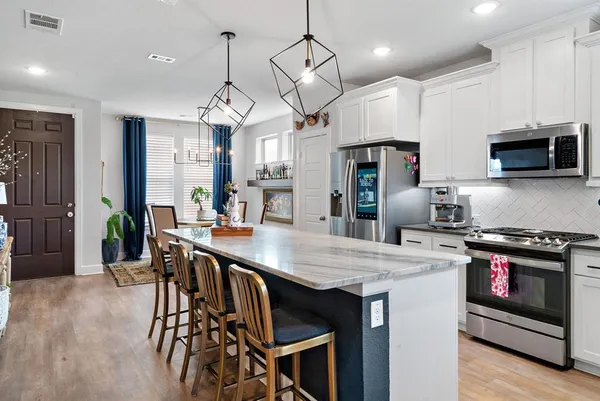 a kitchen with stainless steel appliances a stove a refrigerator a kitchen island a sink cabinets and wooden floor