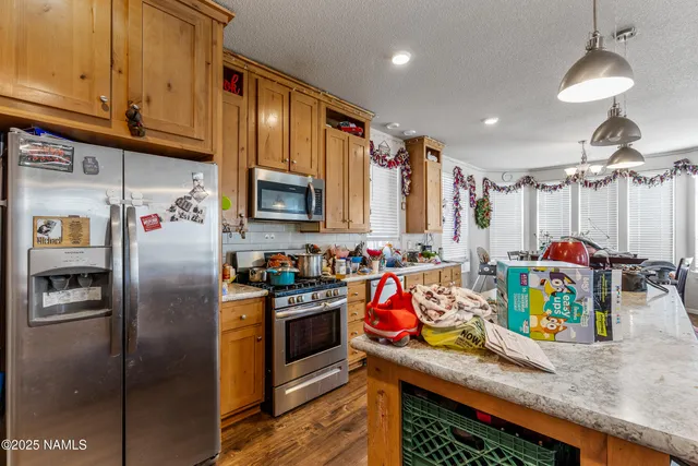 a kitchen with stainless steel appliances granite countertop a refrigerator a stove a sink a dining table and chairs with wooden floor