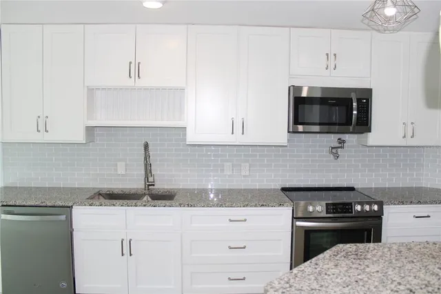 a kitchen with granite countertop white cabinets and black stainless steel appliances