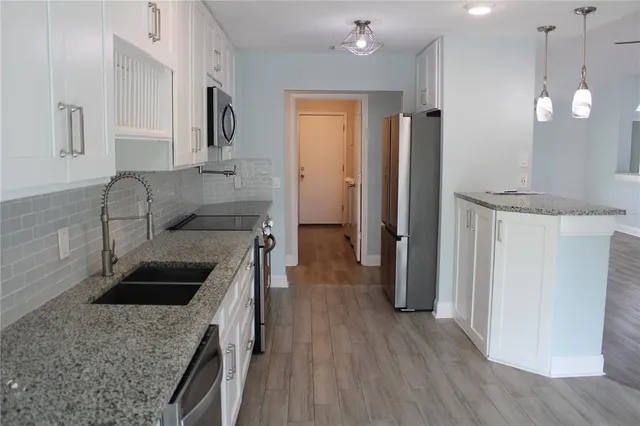 a kitchen with granite countertop a refrigerator a sink dishwasher and a stove with wooden floor