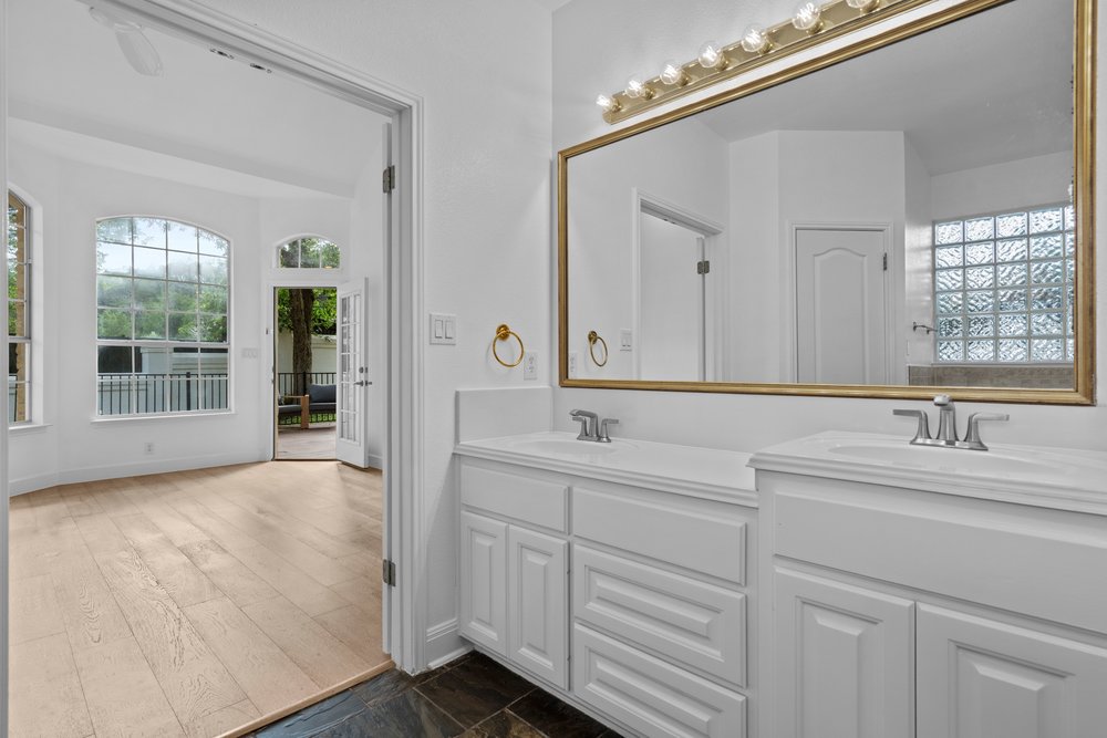 1815 Rue De St Tropez Austin, TX 78746 - Photo 31 of 40 Dual sink vanity with white cabinetry and chrome fixtures, featuring a large framed mirror with overhead vanity lighting