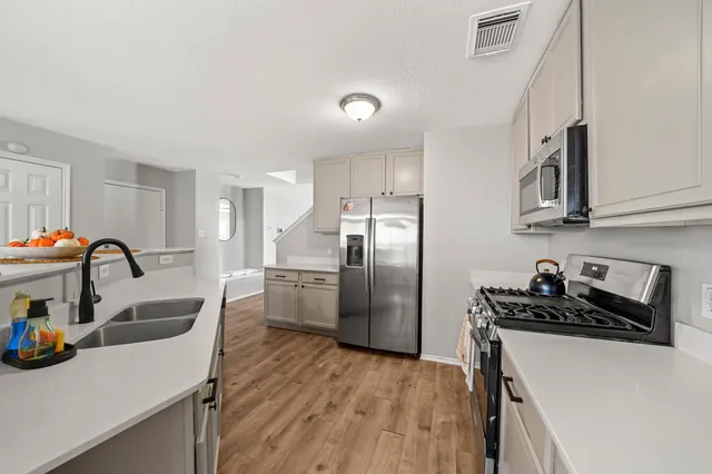 a kitchen with stainless steel appliances granite countertop a sink dishwasher a refrigerator and a stove with wooden floor