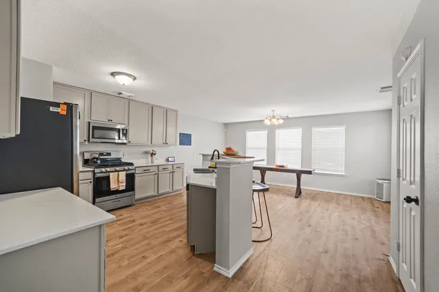 a kitchen with stainless steel appliances a stove a sink a refrigerator white cabinets and wooden floor