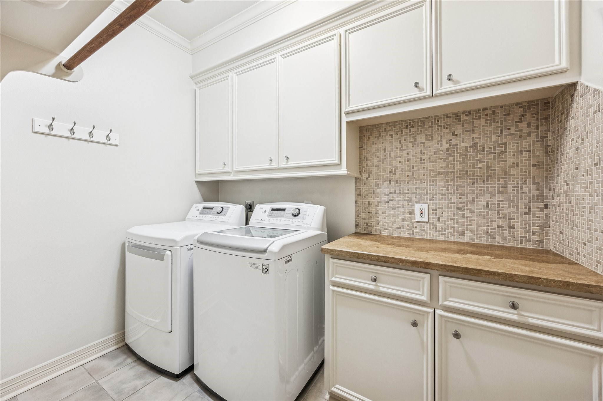 5823 Augusta Court Houston, TX 77057 - Photo 41 of 44 This laundry room features modern appliances, ample cabinetry, a decorative tile backsplash, and a countertop for folding clothes. It also includes a row of hooks for additional storage.