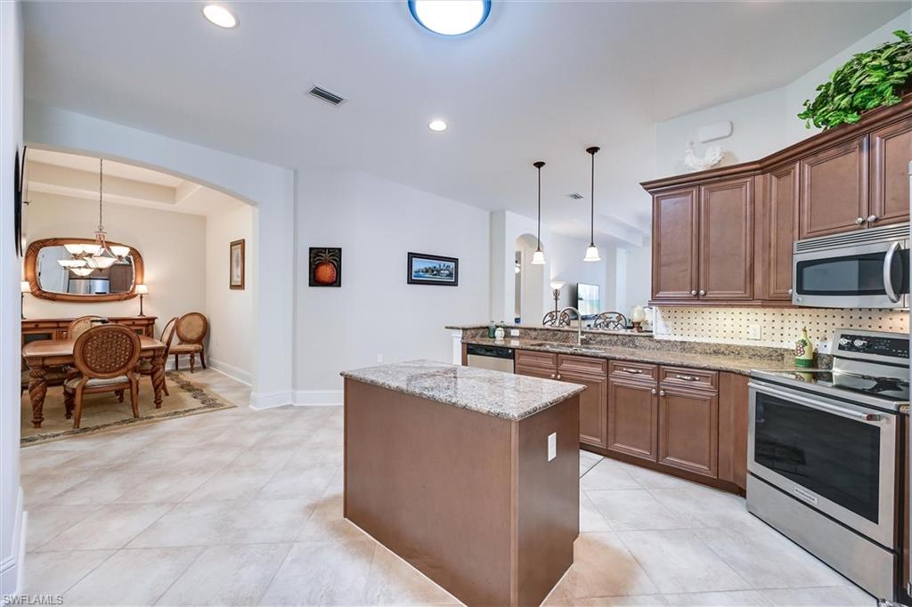 7587 Moorgate Point Way Naples, FL 34113 - Photo 26 of 47 a kitchen with stainless steel appliances granite countertop a stove top oven a sink dishwasher and a refrigerator with wooden cabinets