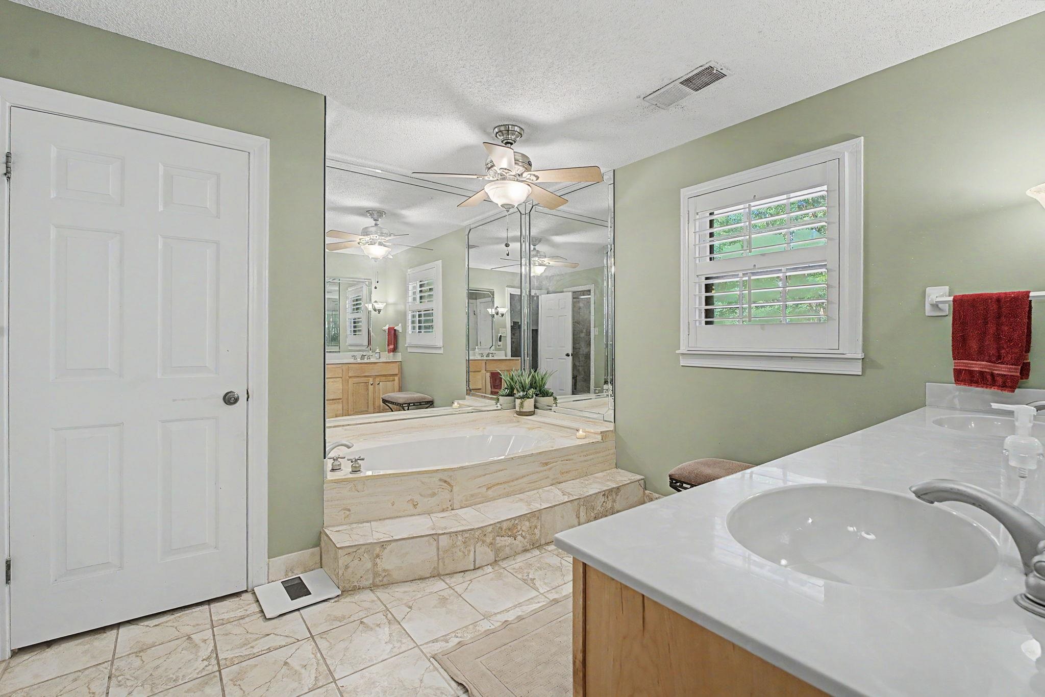 1929 Miller Farms Road Germantown, TN 38138 - Photo 21 of 40 Spacious bathroom featuring a built-in jetted tub with tiled surround, dual vanity with undermount sinks and light-toned countertops, large wall-mounted mirrors, and tiled flooring