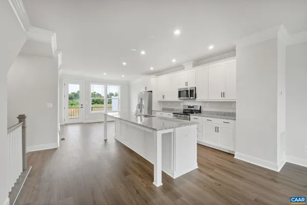a kitchen with stainless steel appliances granite countertop a stove top oven a sink a refrigerator white cabinets and wooden floor