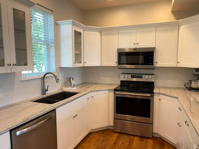 776 Canyon Road Hyde Park, UT 84318 - Photo 5 of 57 Kitchen featuring white cabinetry, stainless steel appliances, patterned backsplash, undermount sink, and wood-finish flooring