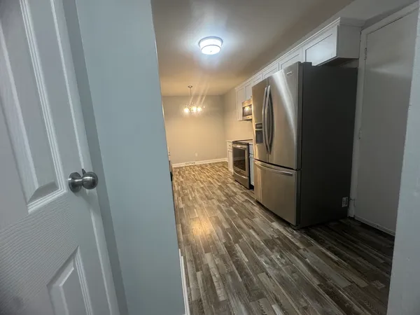 a view of a refrigerator in kitchen and an empty room with wooden floor