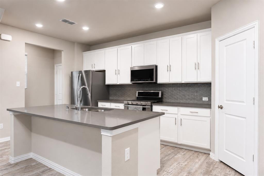 3704 Banton Street Rowlett, TX 75089 - Photo 7 of 16 Kitchen featuring a central island with an integrated sink, stainless steel appliances, white cabinetry, a gray countertop, and wood-finish flooring