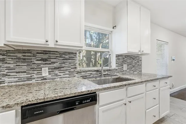 a kitchen with granite countertop a sink and a white wooden cabinets