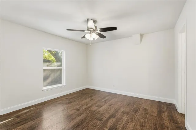 an empty room with wooden floor ceiling fan and windows