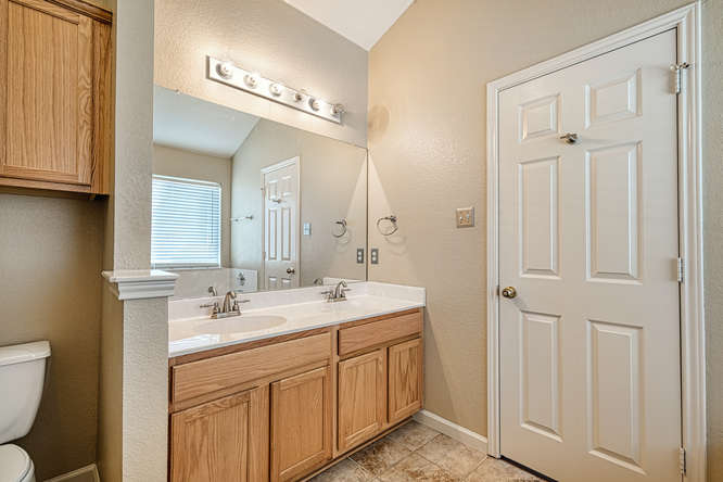 205 Polk Kyle, TX 78640 - Photo 11 of 22 Dual vanity with integrated sinks, wood-finish cabinetry, and a large wall-mounted mirror