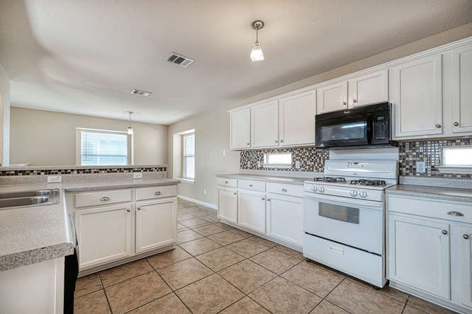 205 Polk Kyle, TX 78640 - Photo 7 of 22 Kitchen featuring white cabinetry, a black over-the-range microwave, a white gas range, and a mosaic tile backsplash