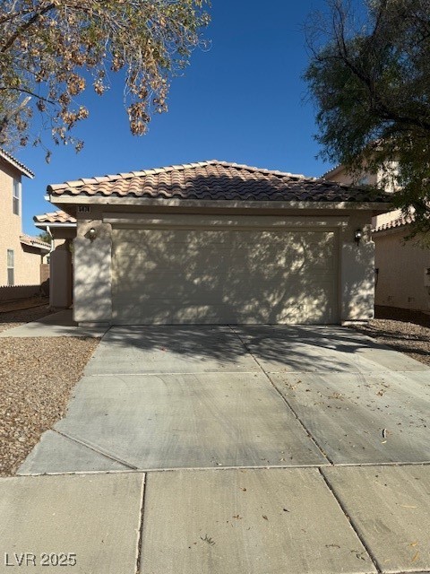 View of front facade with a tile roof, driveway, stucco siding, and an attached garage