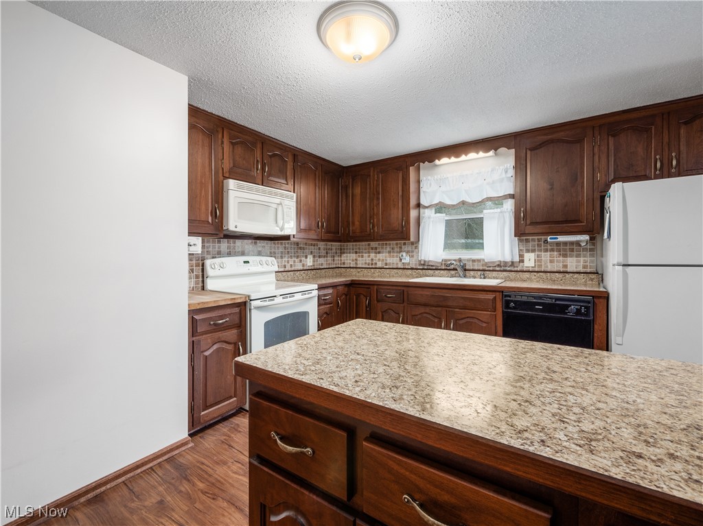 12454 Old Rainer Road Roseville, OH 43777 - Photo 9 of 33 Kitchen with sink, white appliances, backsplash, dark brown cabinets, and dark hardwood / wood-style flooring