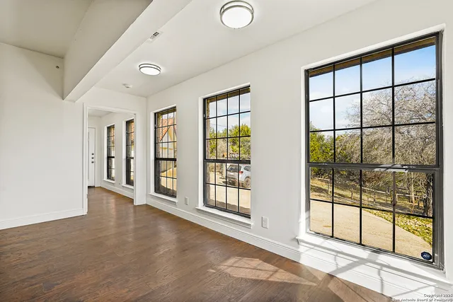 an empty room with wooden floor chandelier fan and windows