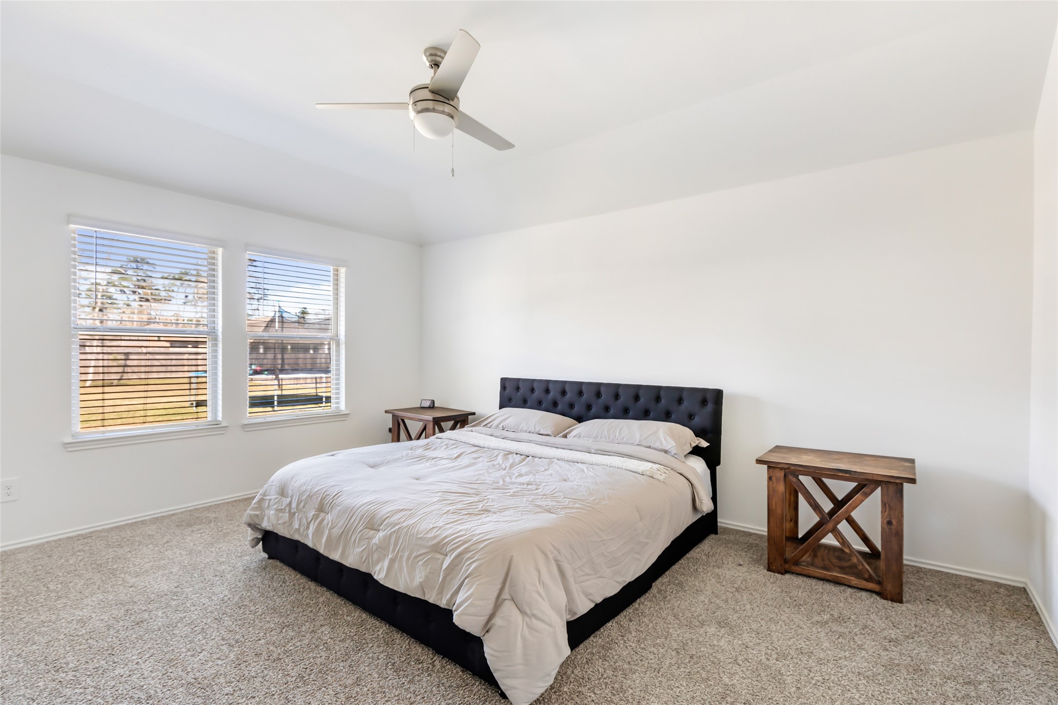 811 Republic Road New Caney, TX 77357 - Photo 32 of 37 This bedroom features a comfortable layout with a large bed, neutral carpeting, and ample natural light from two windows. It includes a ceiling fan and simple wooden side tables, creating a cozy and functional space.