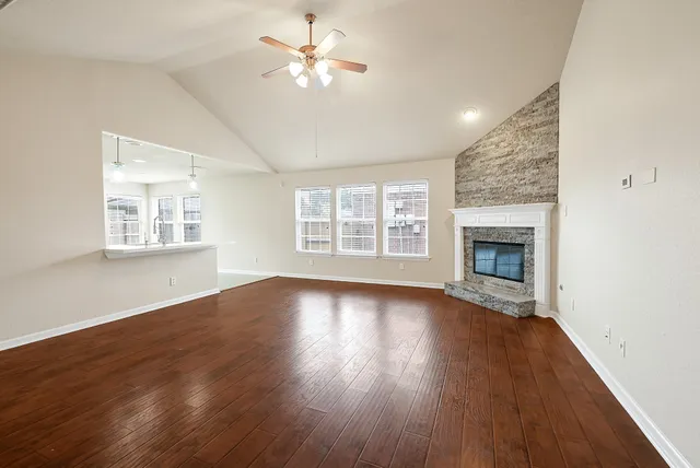 an empty room with wooden floor fireplace and windows