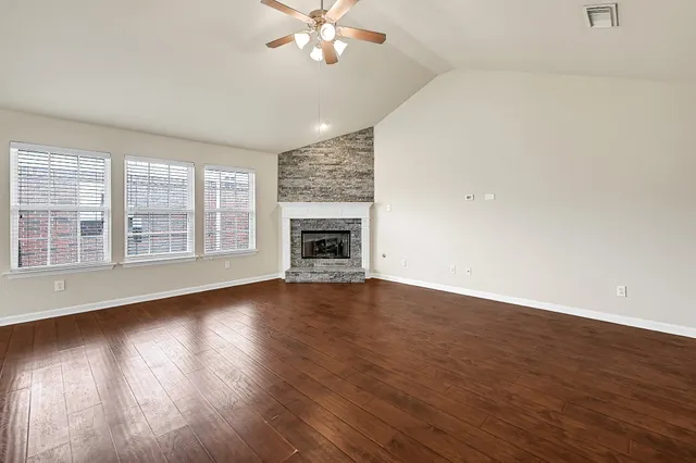 an empty room with wooden floor fan and windows