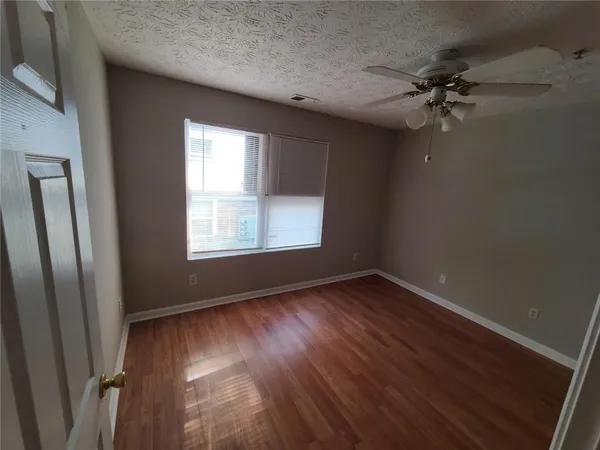an empty room with wooden floor fan and windows