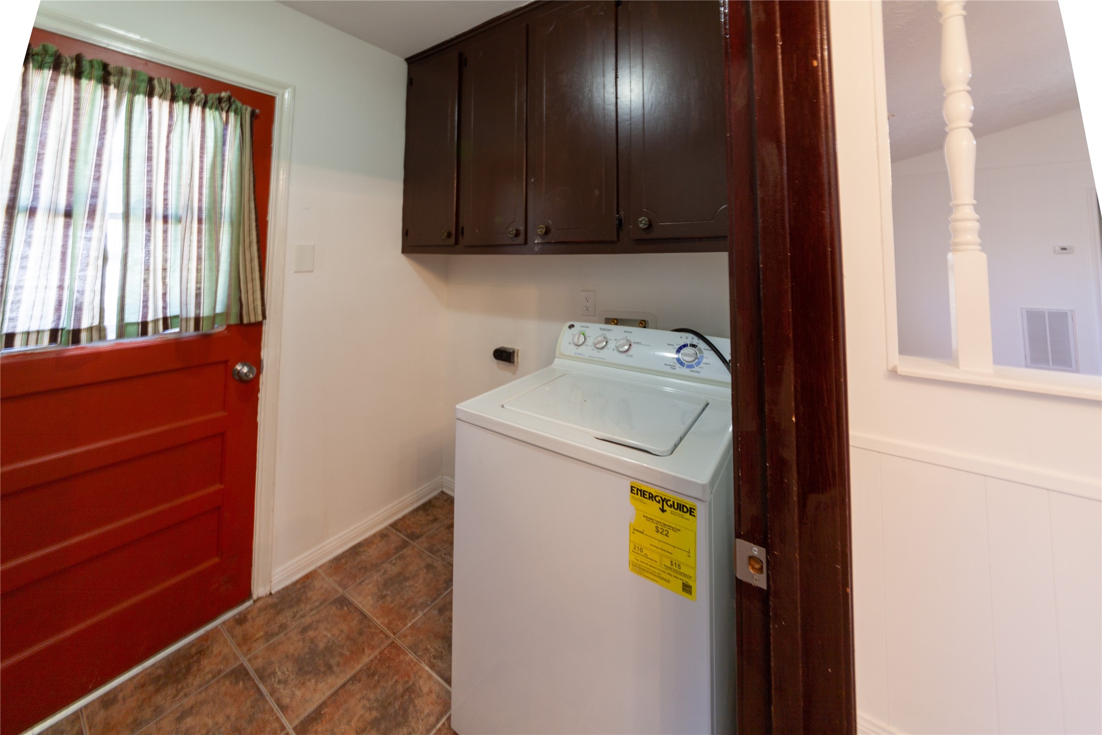 8826 Roos Road Houston, TX 77036 - Photo 33 of 42 Compact laundry area with a washing machine beneath dark wood cabinets. It features a tiled floor and a red door with a window, adding a pop of color and natural light.