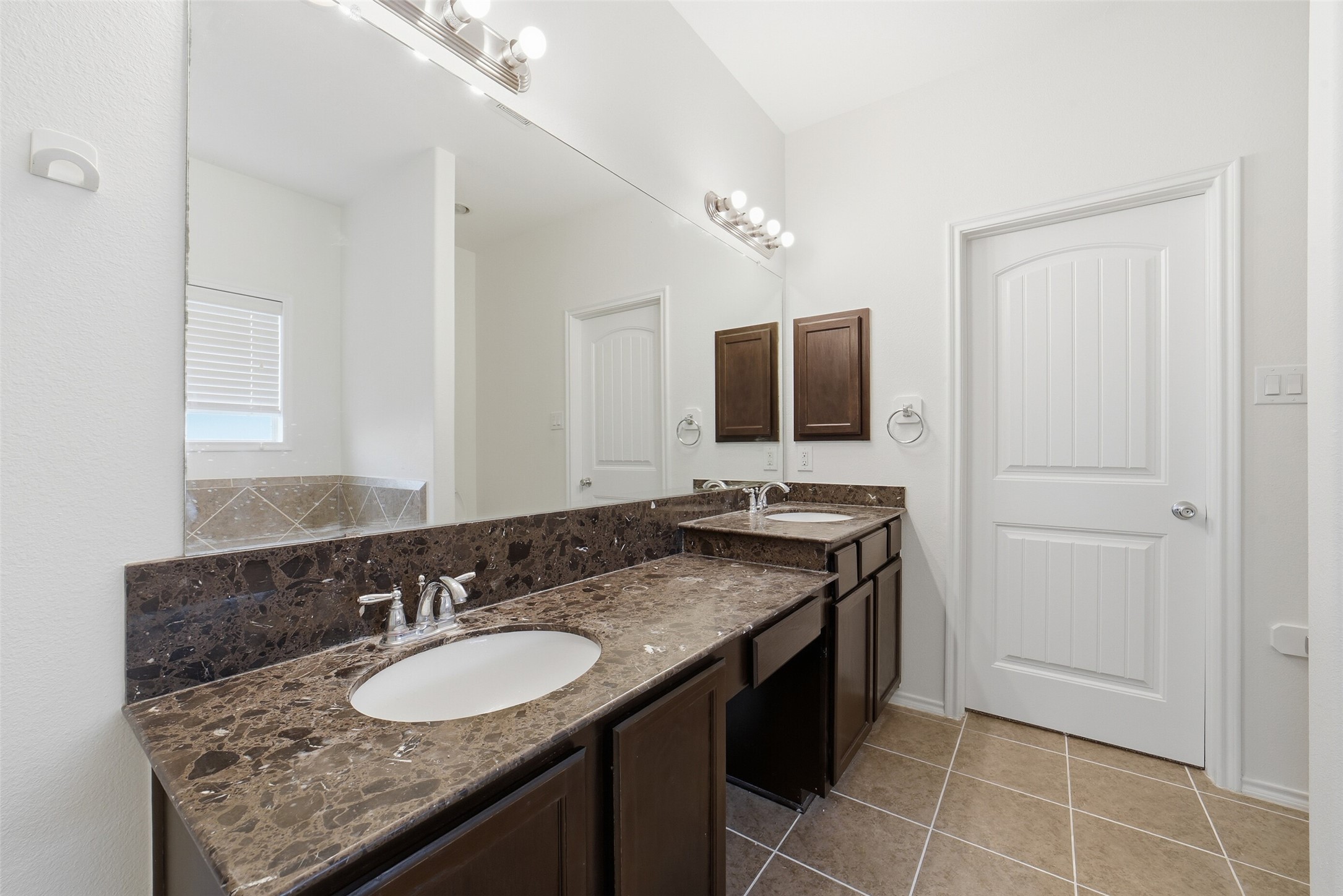 12830 Spruce Circle Tomball, TX 77375 - Photo 23 of 39 This primary bathroom features
a dual-sink, with a built in
vanity. Elegant dark marble
countertops and wood
cabinetry. It has a large mirror,
bright lighting, and a neutral tile
floor, creating a spacious and
modern feel.