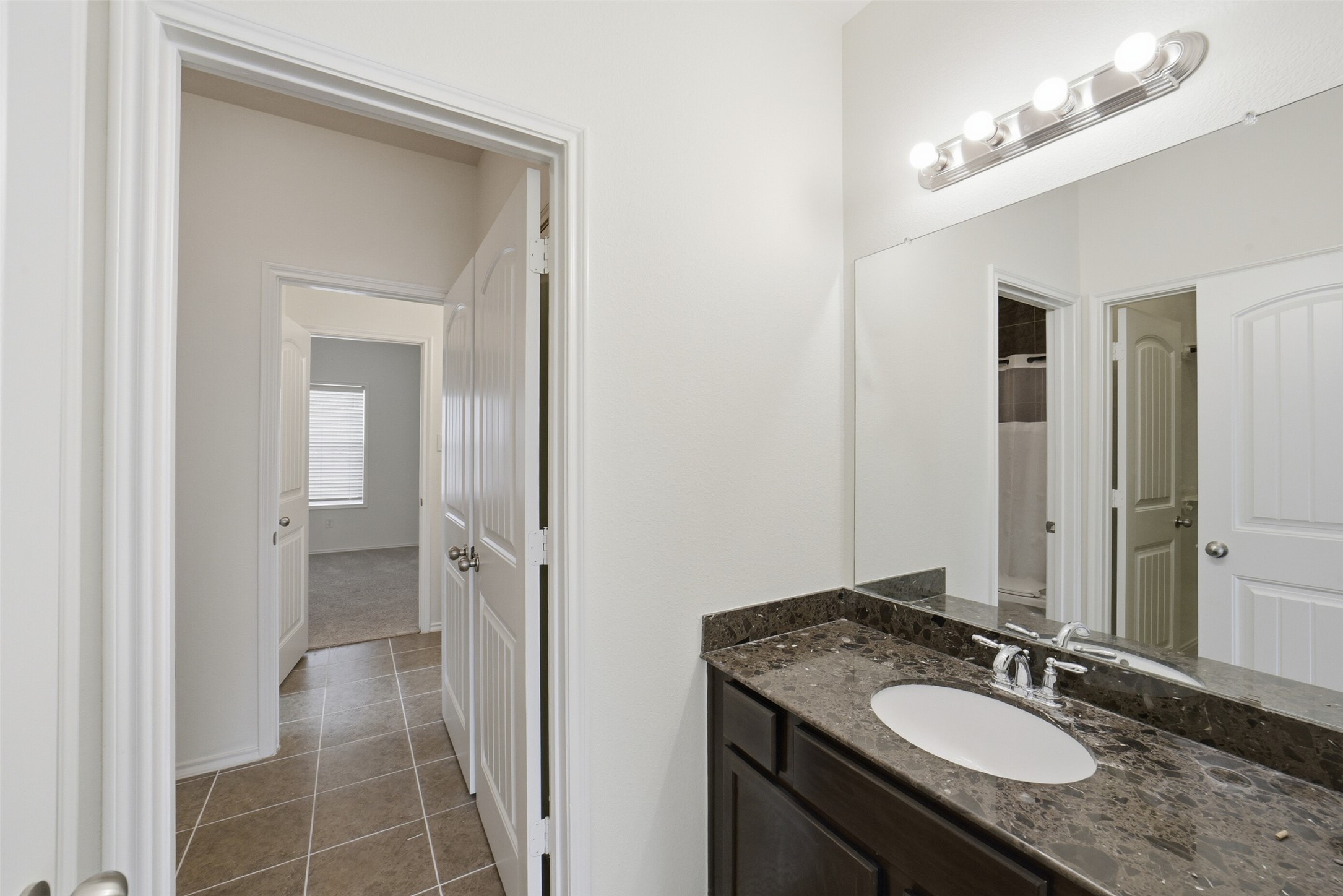 12830 Spruce Circle Tomball, TX 77375 - Photo 29 of 39 A photo that shows the ensuite
Jack and Jill bathroom off from
the secondary bedroom with a
dark marble countertop and
sink with plenty of light
illuminating the large mirror.
Features dark brown wood
cabinets and drawers.