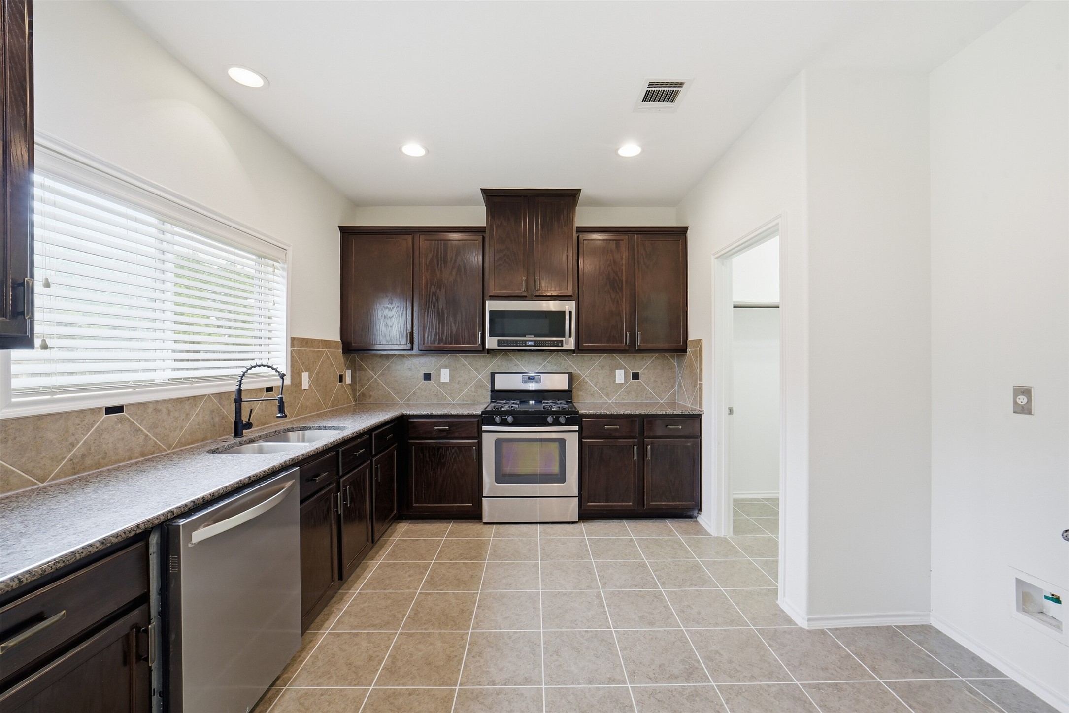 12830 Spruce Circle Tomball, TX 77375 - Photo 7 of 39 This kitchen features dark
wood cabinetry, stainless steel
appliances, and beige tile
flooring. It has a modern look
with ample counterspace, a
tiled backsplash, and natural
light from a large window.