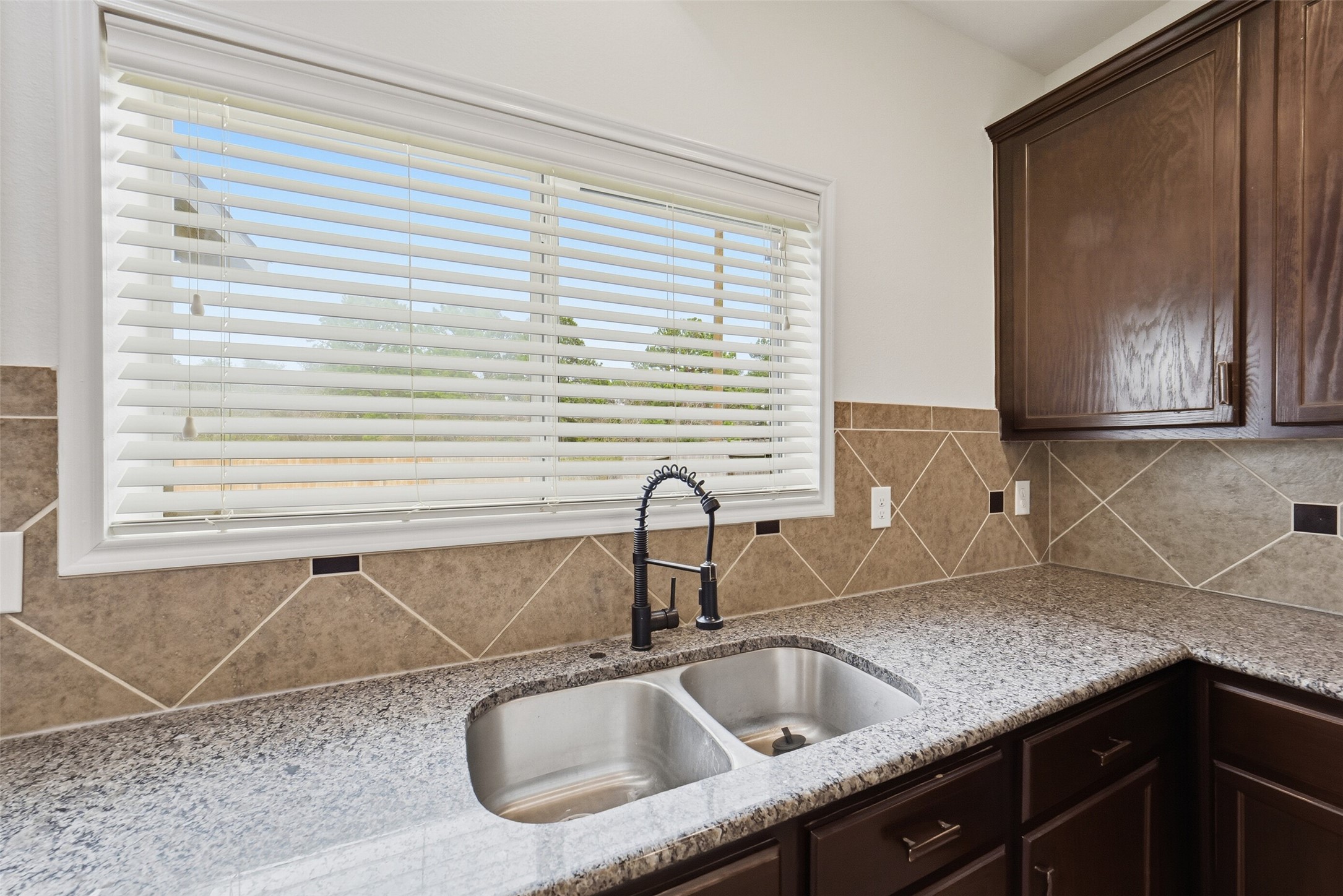 12830 Spruce Circle Tomball, TX 77375 - Photo 9 of 39 This kitchen features granite
countertops, a double stainless
steel sink with a modern faucet,
and dark wood cabinets. The
backsplash is a neutral tile with
a decorative pattern, and a
large window provides natural
light.