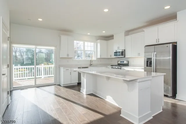 a kitchen with stainless steel appliances granite countertop a sink a stove a refrigerator with white cabinets and wooden floor