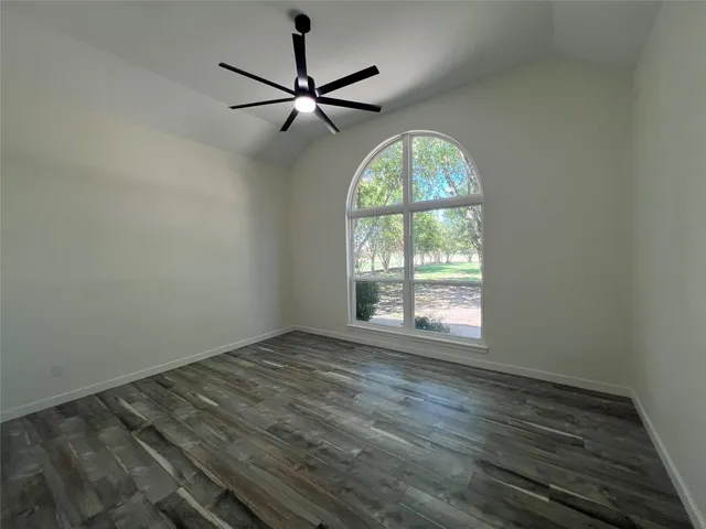 an empty room with wooden floor fan and windows