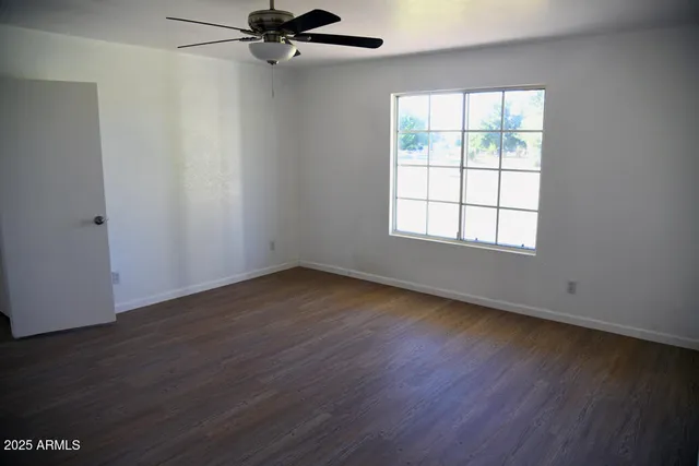 an empty room with wooden floor fan and windows