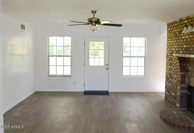 an empty room with wooden floor chandelier fan and windows