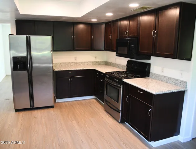 a kitchen with stainless steel appliances kitchen island granite countertop a refrigerator a sink and wooden cabinets