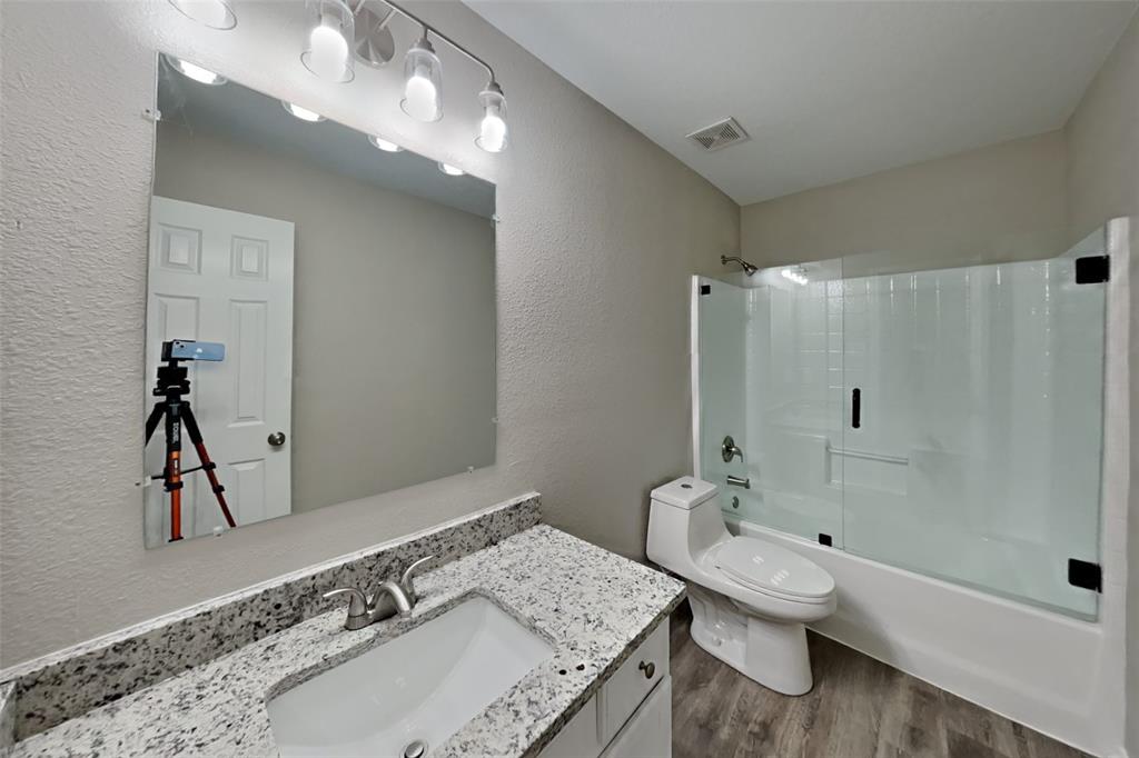 4204 Highgate Road Fort Worth, TX 76244 - Photo 16 of 19 Bathroom featuring a textured wall, bath / shower combo with glass door, vanity, and dark wood finished floors
