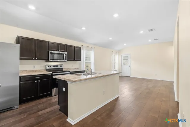 a kitchen with stainless steel appliances granite countertop a stove top oven a sink dishwasher and a refrigerator with wooden floor