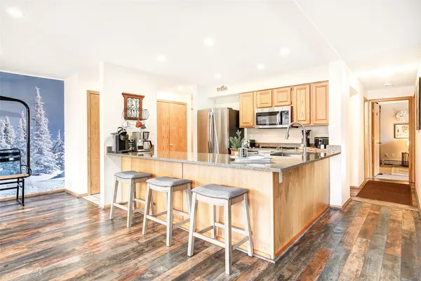 a kitchen with stainless steel appliances kitchen island granite countertop a stove top oven a sink dishwasher and a dining table with wooden floor