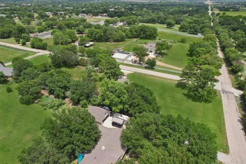 an aerial view of a residential houses with outdoor space and trees all around