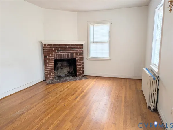 an empty room with wooden floor fireplace and windows