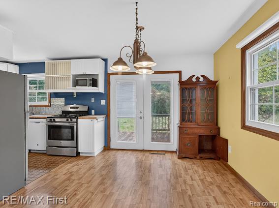 56375 Bates Road New Baltimore, MI 48051 - Photo 17 of 35 Open-concept living space featuring a wood-finish plank floor throughout, a blue-painted kitchen with white cabinetry and stainless steel appliances, pendant lighting, French doors leading to an outdoor deck, large multi-pane windows flooding the space with natural light, and a built-in wooden cabinet with glass-front doors