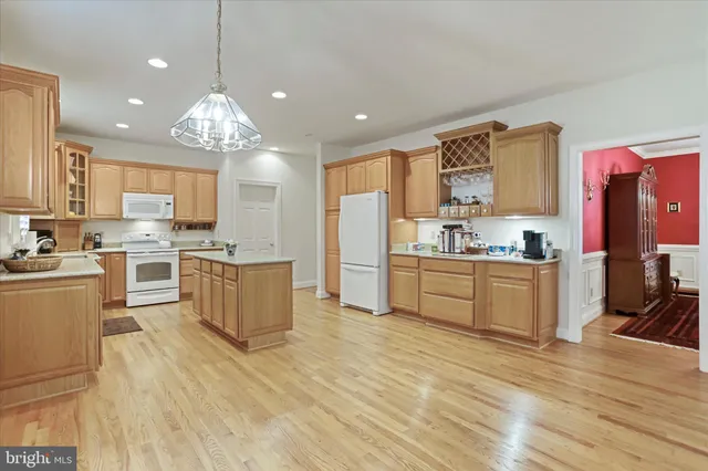 a large kitchen with kitchen island a stove a sink dishwasher a refrigerator and white cabinets with wooden floor