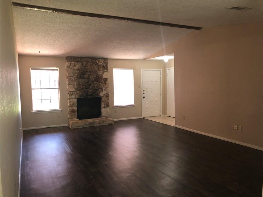 6211 Sunkist Lane Austin, TX 78749 - Photo 2 of 8 Spacious living area featuring wood-finish flooring, a stone-faced fireplace, two large windows, a vaulted ceiling with exposed beam, and a paneled entry door