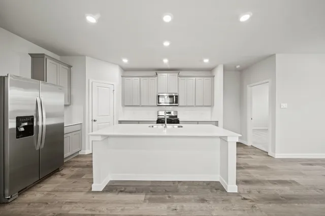 a view of a kitchen with kitchen island stainless steel appliances refrigerator stove and wooden floor