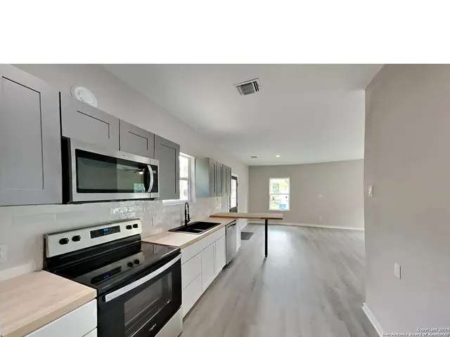 a kitchen with a stove a sink and a flat screen tv