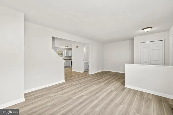 a view of empty room with wooden floor and kitchen